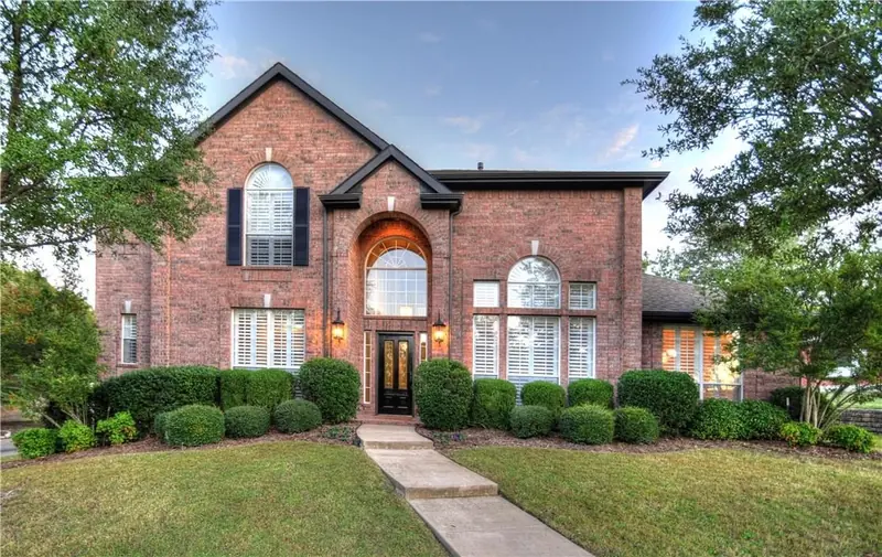 The same brick home in daylight, framed by trees